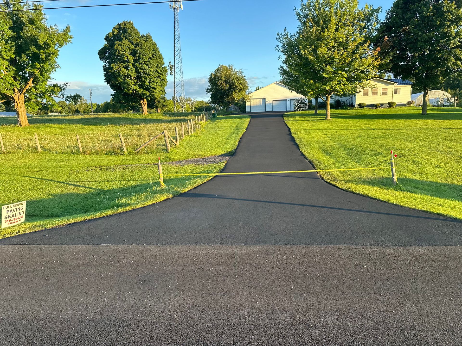 A driveway going through a grassy field with a house in the background
