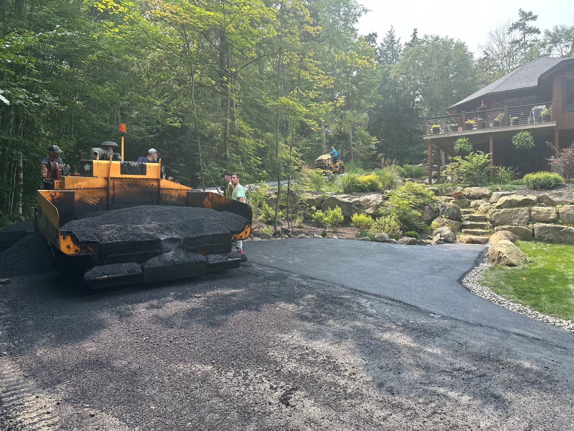 A machine is laying asphalt on a driveway in front of a house.