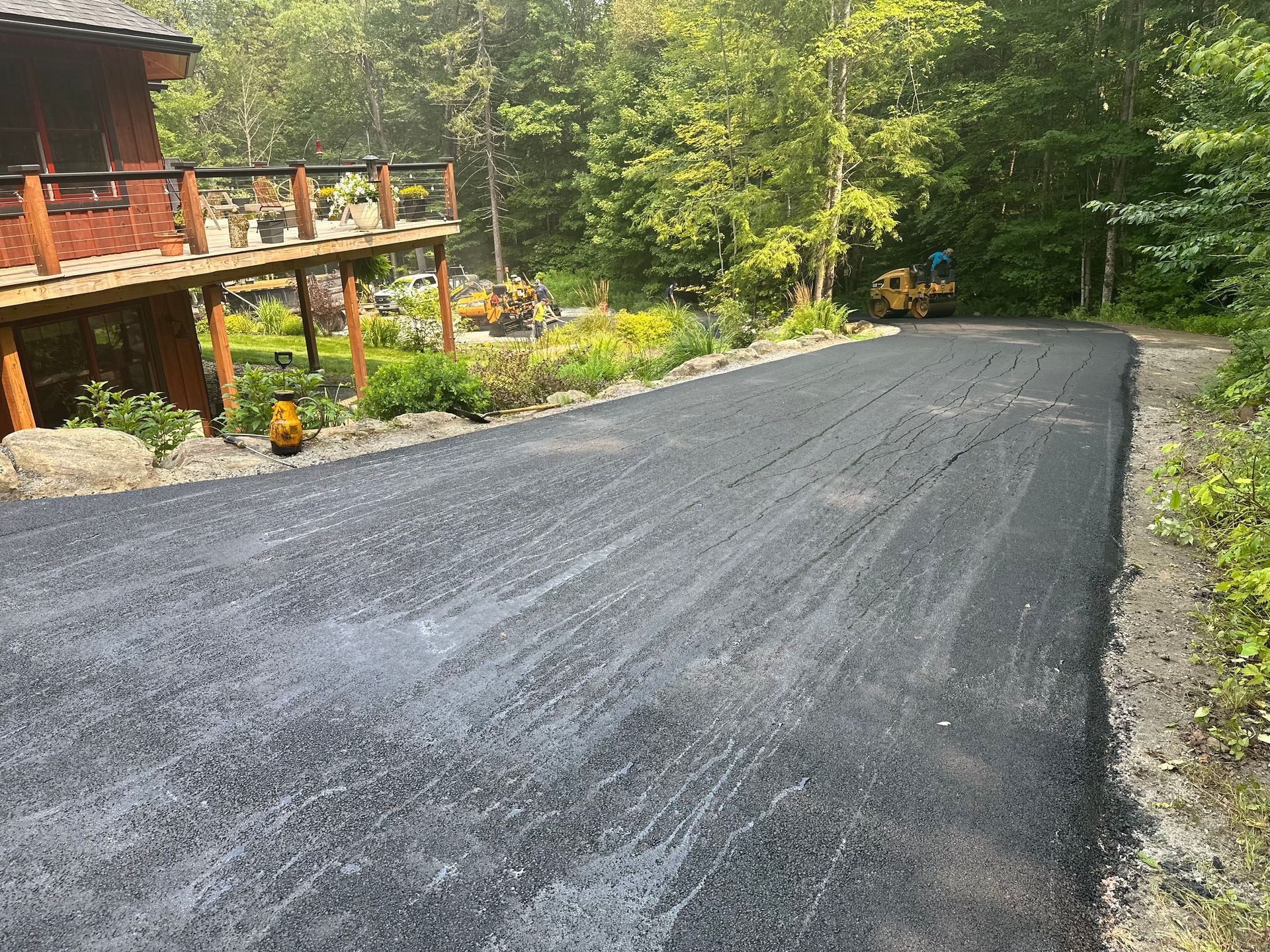 A asphalt driveway leading to a house in the woods.