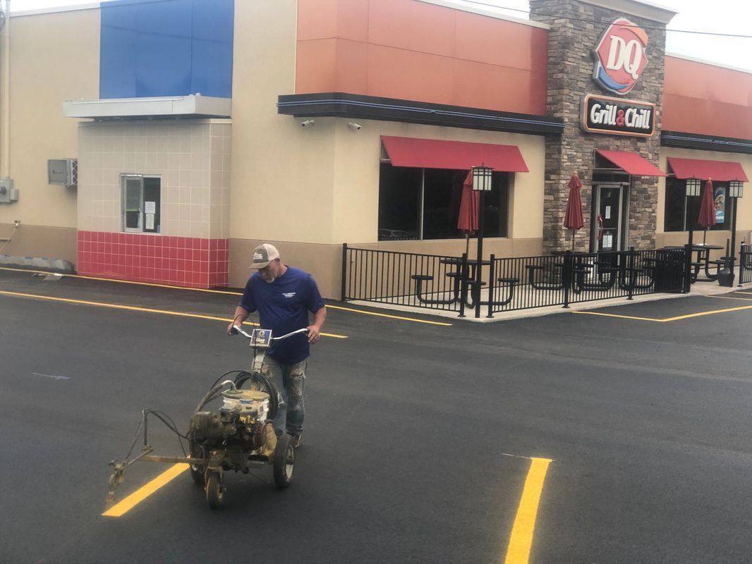 A man is painting a parking lot in front of a dairy queen restaurant.