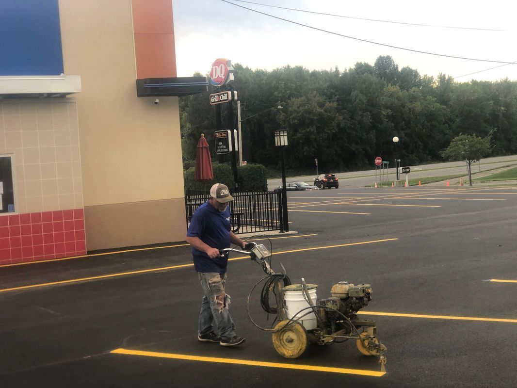 A man is using a machine to paint a yellow line in a parking lot.