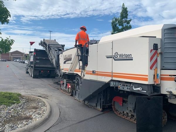 A man is standing on top of a machine that is laying asphalt.