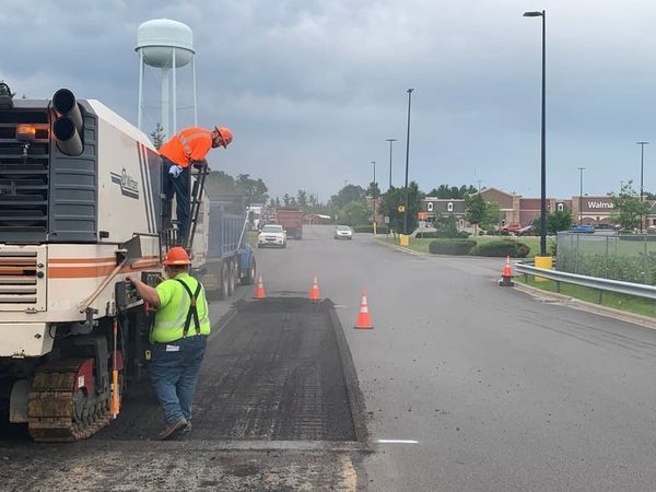 Two construction workers are working on a road with a water tower in the background
