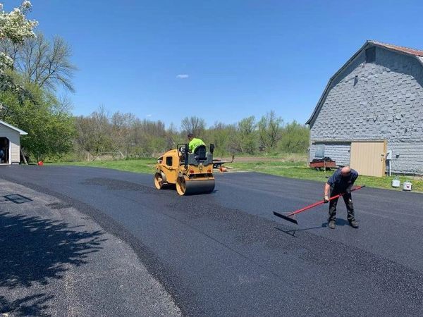 A man is using a broom to spread asphalt on a road.