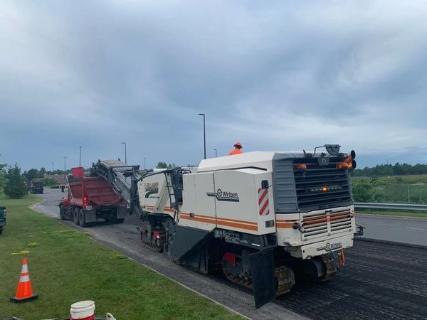 A machine is cutting asphalt on the side of a road.