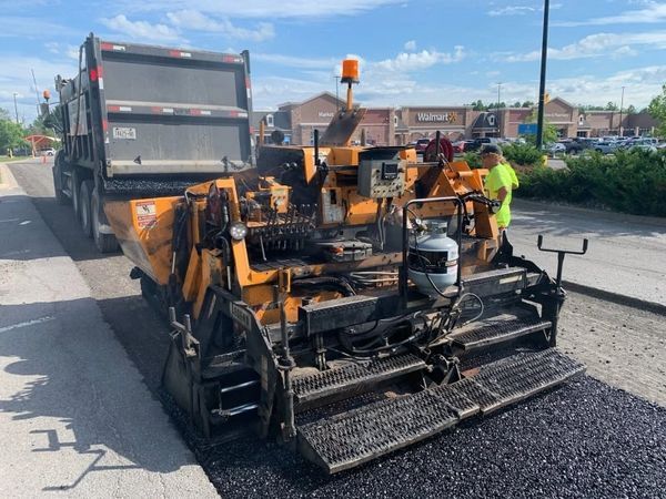A machine is laying asphalt on the side of a road.