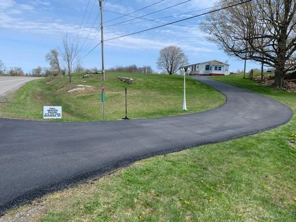 A curvy road going through a grassy field with a house in the background.