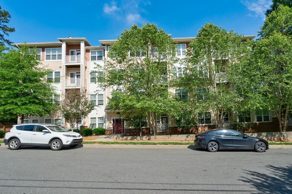 Exterior view of an apartment building with landscaped trees and parked cars.