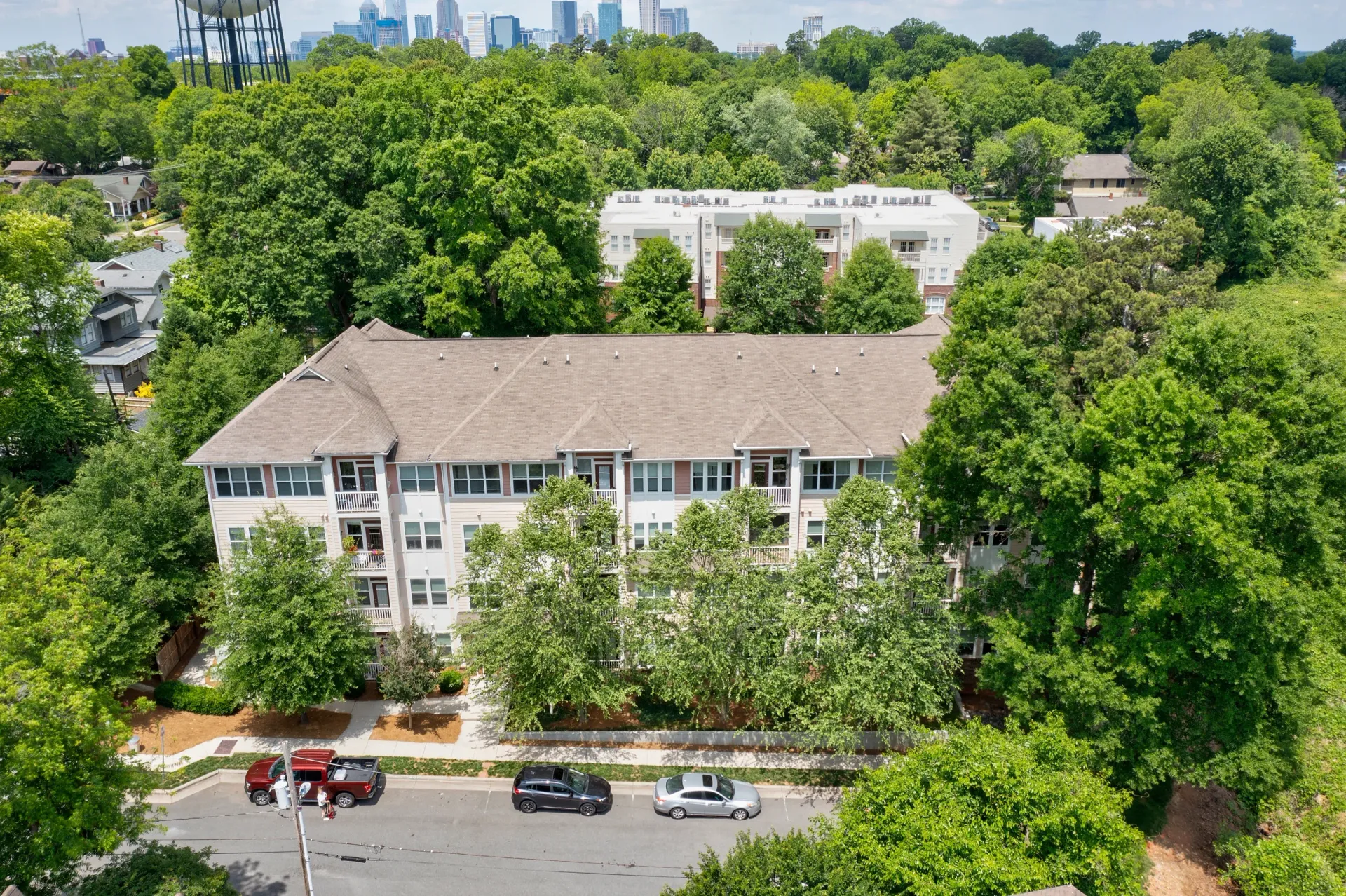 Aerial view of an apartment building surrounded by trees and parked cars.