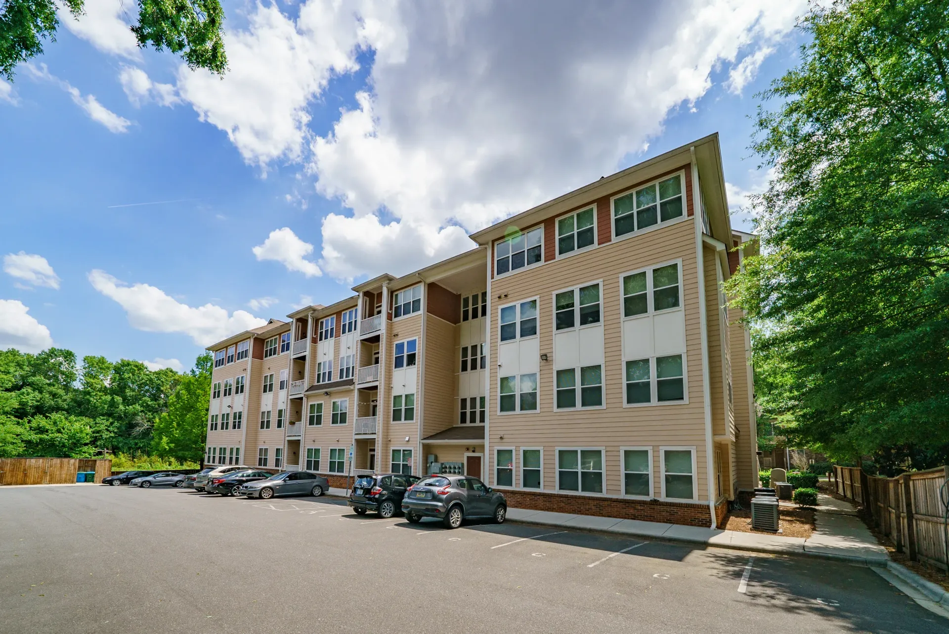 Exterior view of an apartment building with parking area and trees nearby.