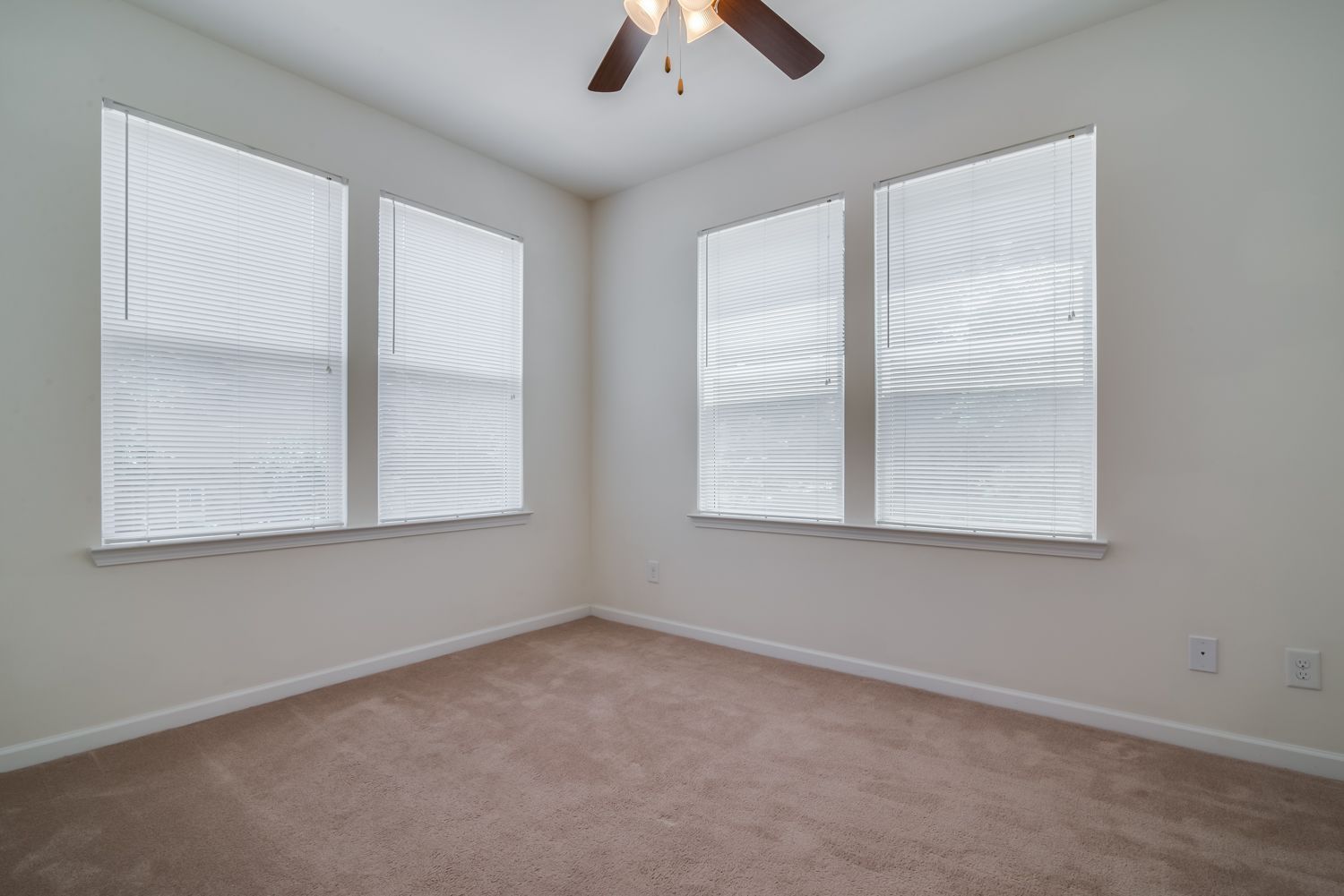 Bright, empty apartment room with two windows and carpet flooring.