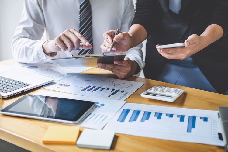 Persona seduta a una scrivania in un ufficio luminoso, con documenti, apparecchiature informatiche e ampie finestre.