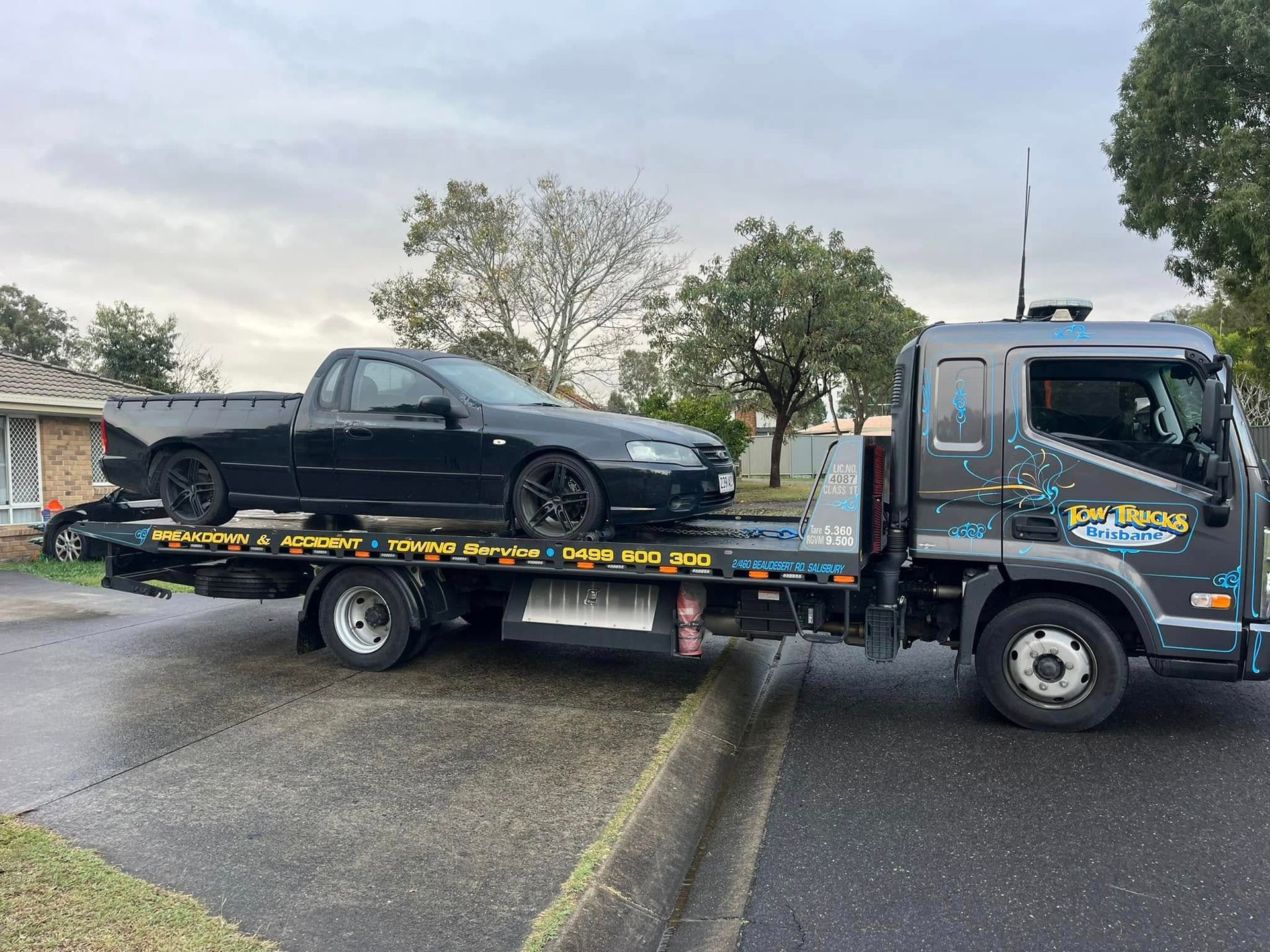 Tow Truck Carrying a Black Sedan on a Flatbed in a Wet Parking Lot — A B & Forge Towing In Caboolture, QLD