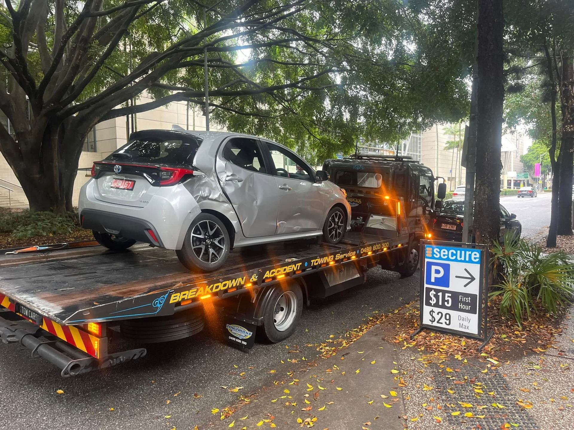 Silver car on a tow truck with rear damage, parked under trees beside a parking sign — A B & Forge Towing In Narangba, QLD