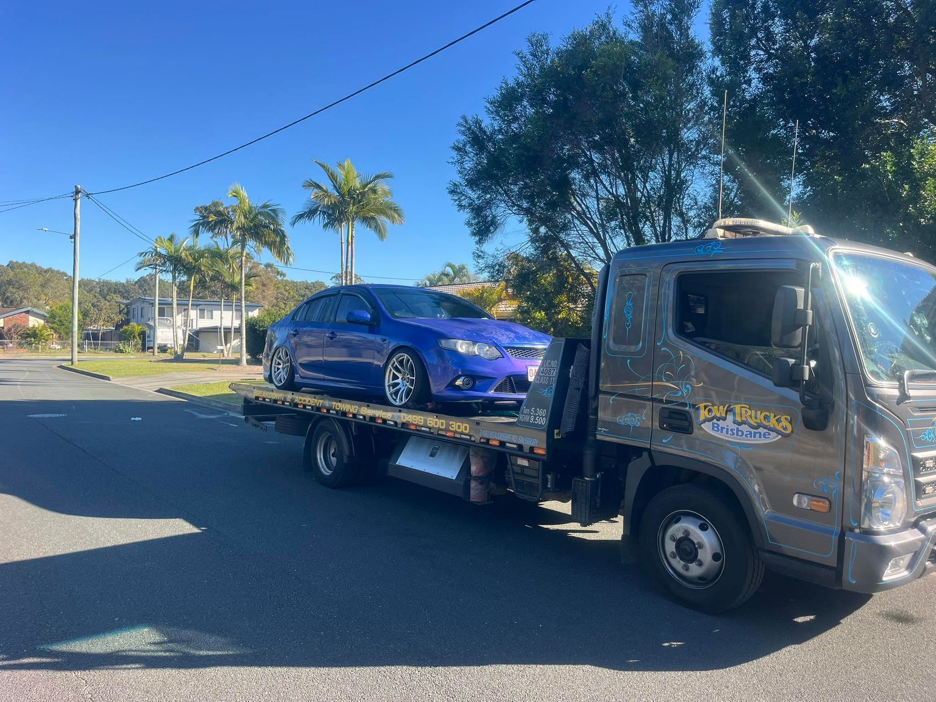 Tow Truck Carrying a Blue Sedan on a Sunny Suburban Street — A B & Forge Towing In Caboolture, QLD