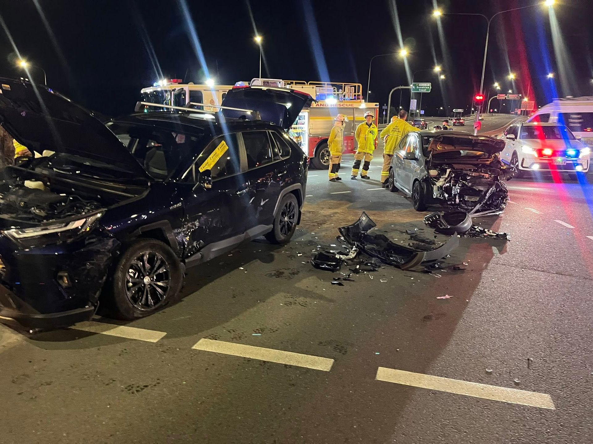 Nighttime multi-vehicle crash on a road, with two damaged cars and emergency responders nearby — A B & Forge Towing In Narangba, QLD