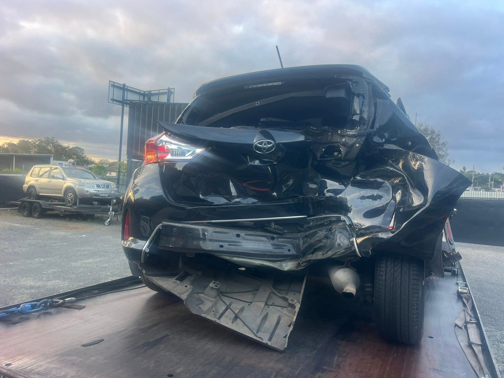 Severely damaged black SUV after a crash, rear end crushed, on a roadway at dusk — A B & Forge Towing In Narangba, QLD
