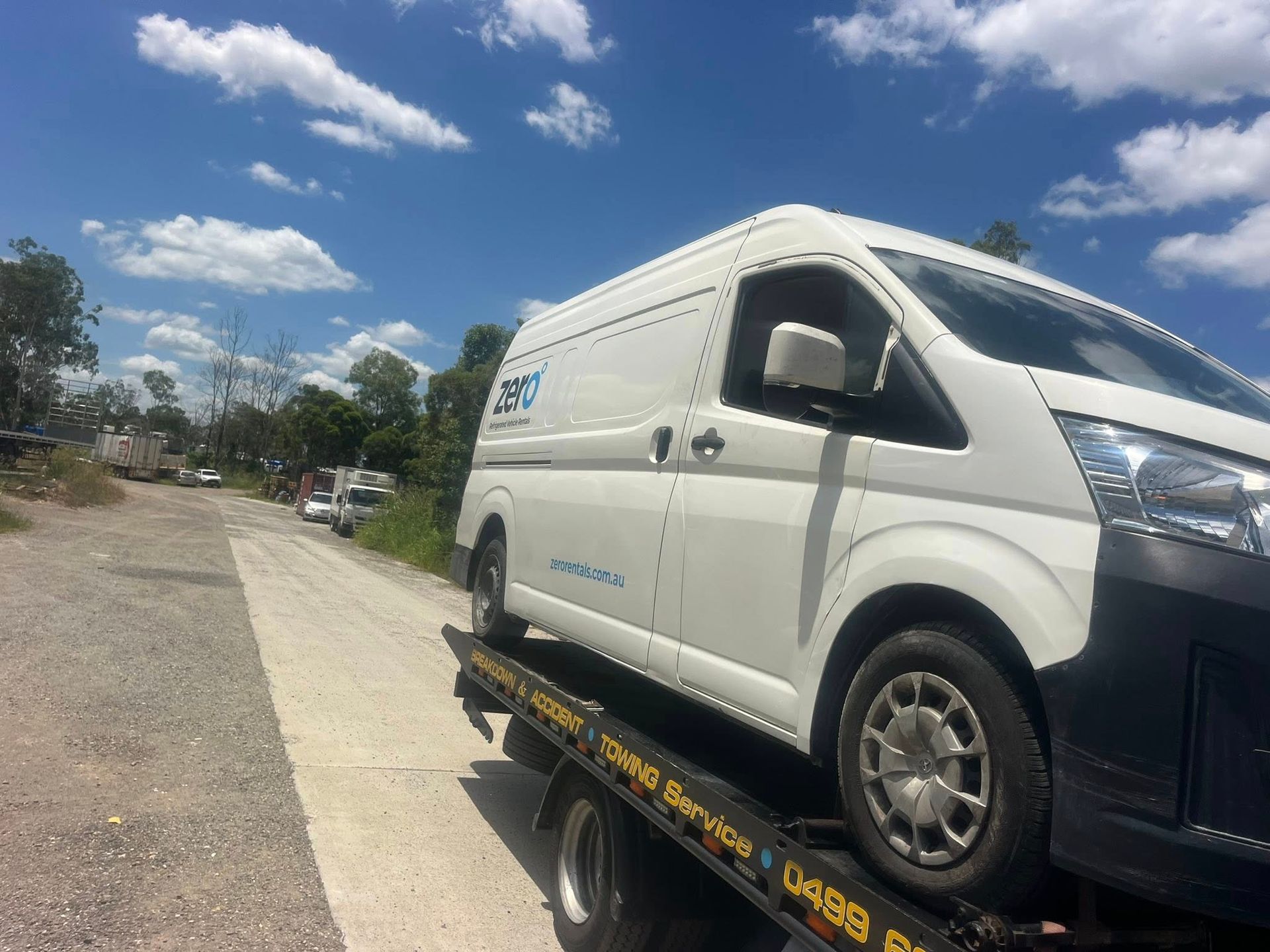 White van on a flatbed tow truck beside a sidewalk under a blue sky with clouds — A B & Forge Towing In Narangba, QLD
