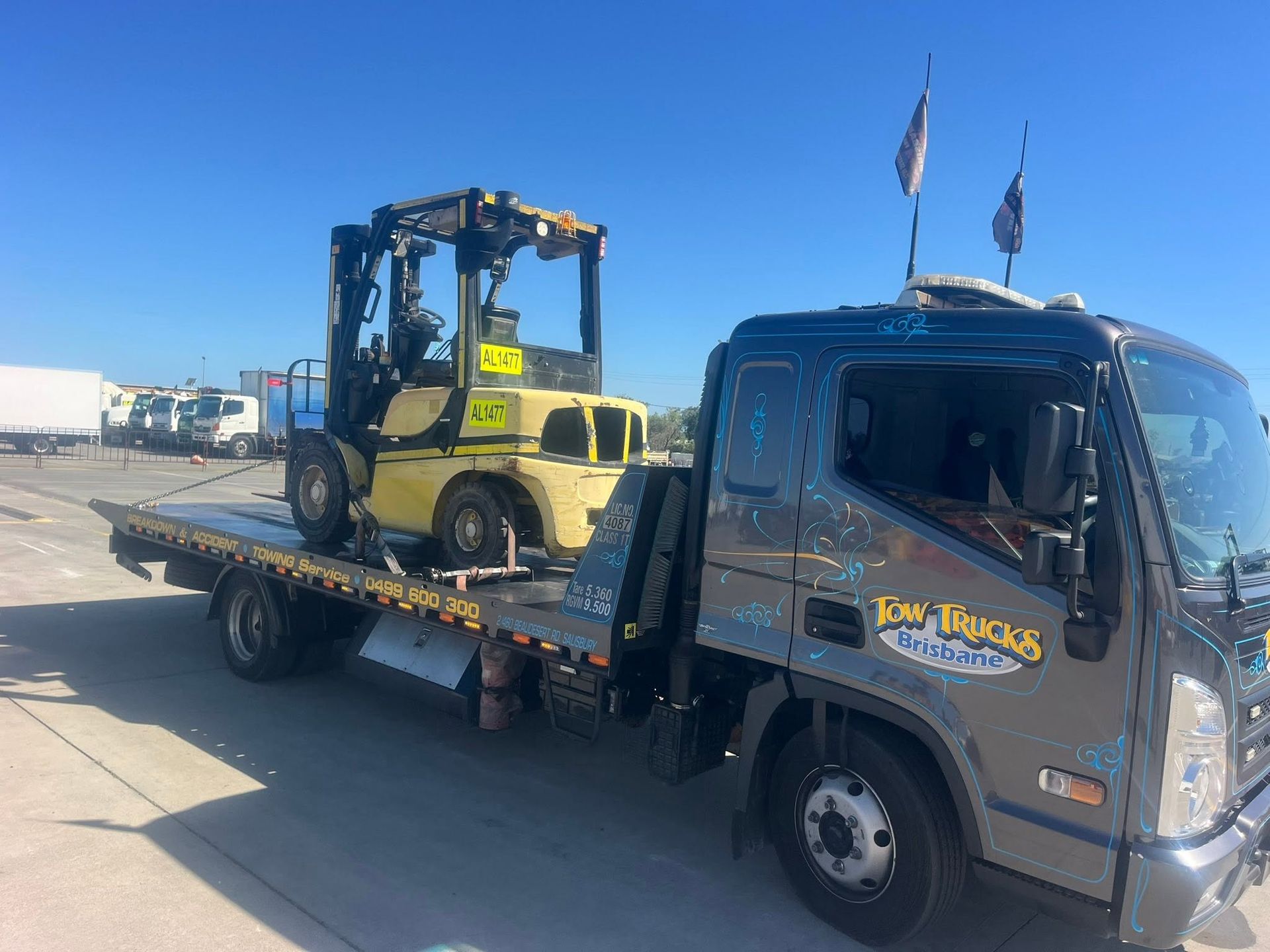 Tow Truck Carrying a Yellow Forklift on a Flatbed Under a Clear Blue Sky — A B & Forge Towing In Bribie Island, QLD