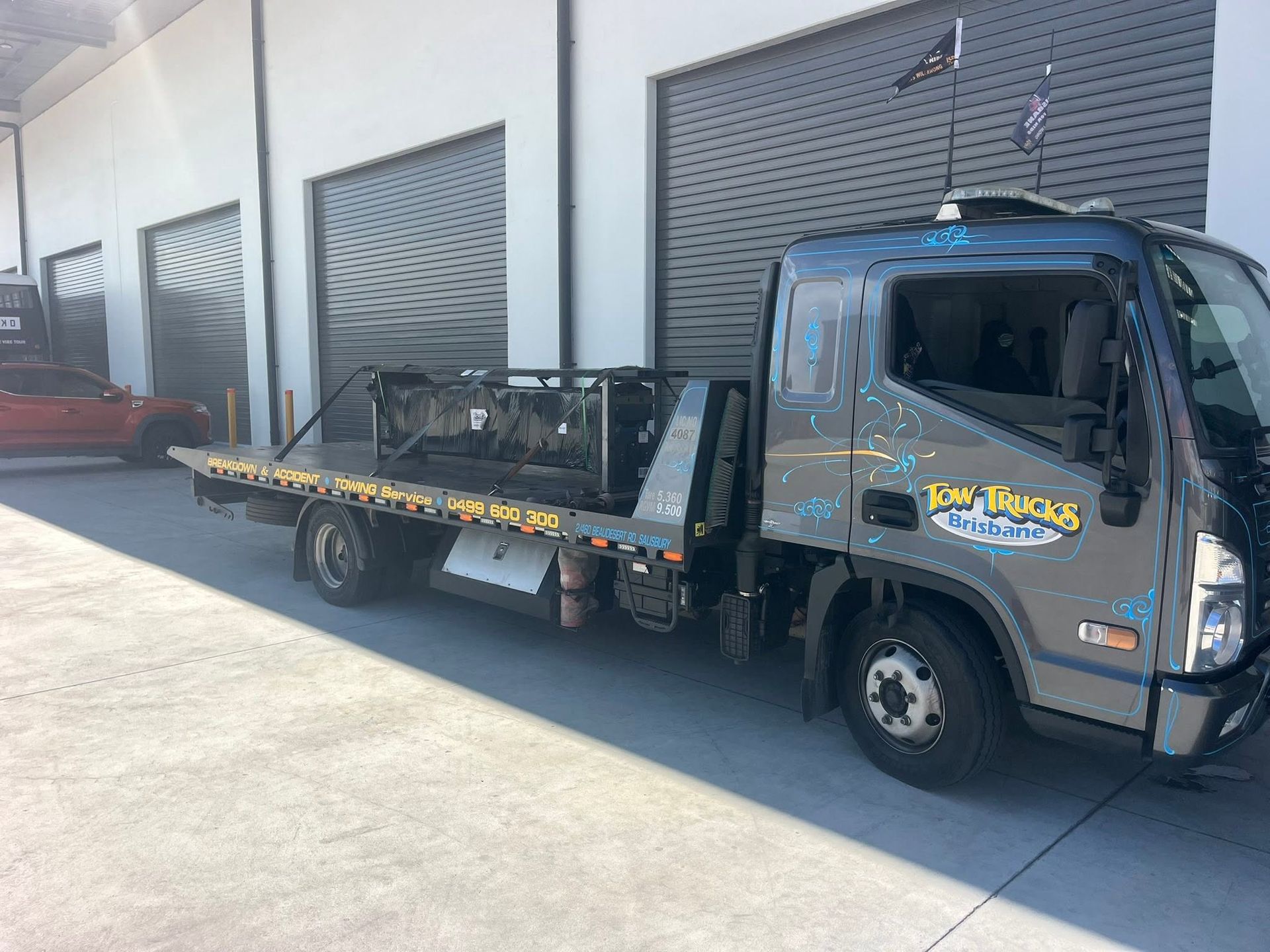 Flatbed Tow Truck Parked Outside Warehouse Doors in Bright Sunlight — A B & Forge Towing In Redcliffe, QLD