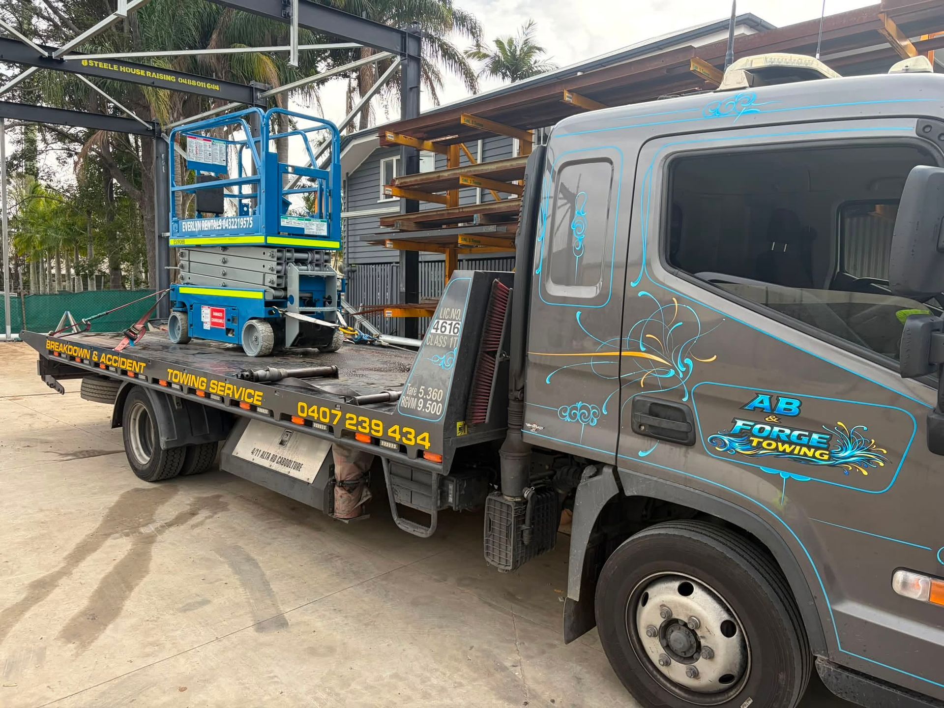 Gray Flatbed Truck Carrying a Blue Scissor Lift Parked Outdoors — A B & Forge Towing In North Lakes, QLD