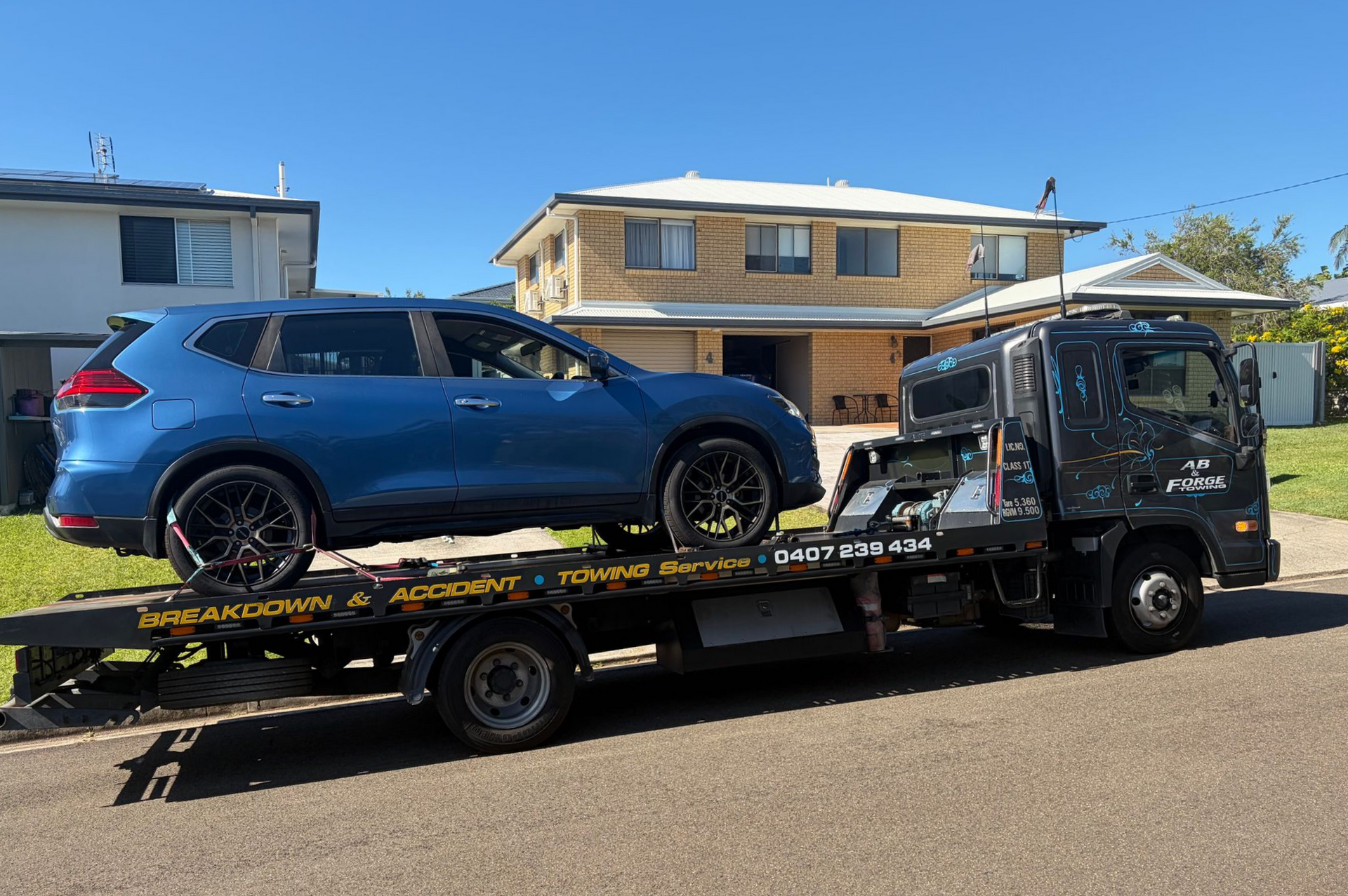 Blue SUV Loaded on a Tow Truck in a Residential Street Under Clear Sky — A B & Forge Towing In Bribie Island, QLD