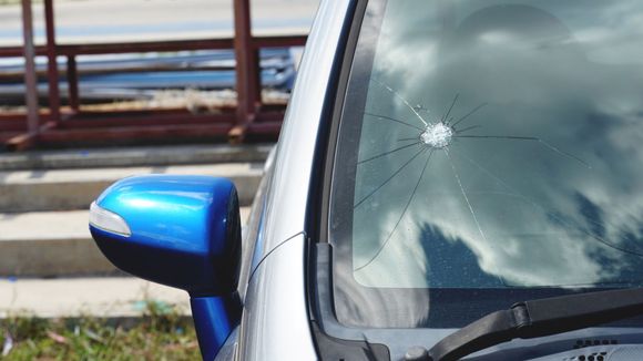 Blue car side mirror and windshield with a cracked impact mark near the top right.