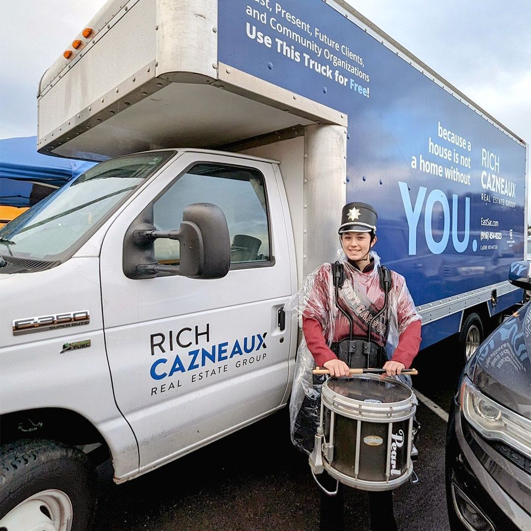 A man is holding a drum in front of Rich Cazneaux Real Estate Group Truck in East Sacramento