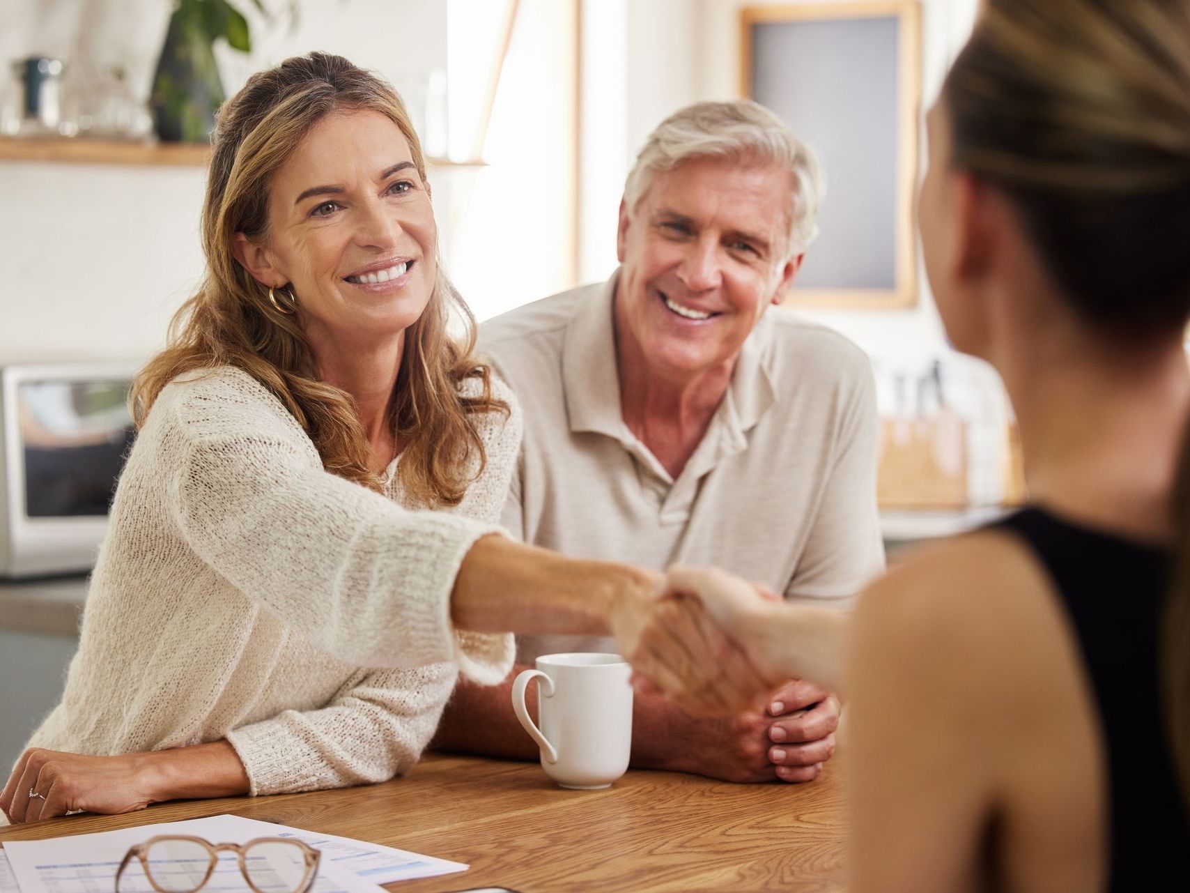 A woman is shaking hands with a man and woman while sitting at a table.