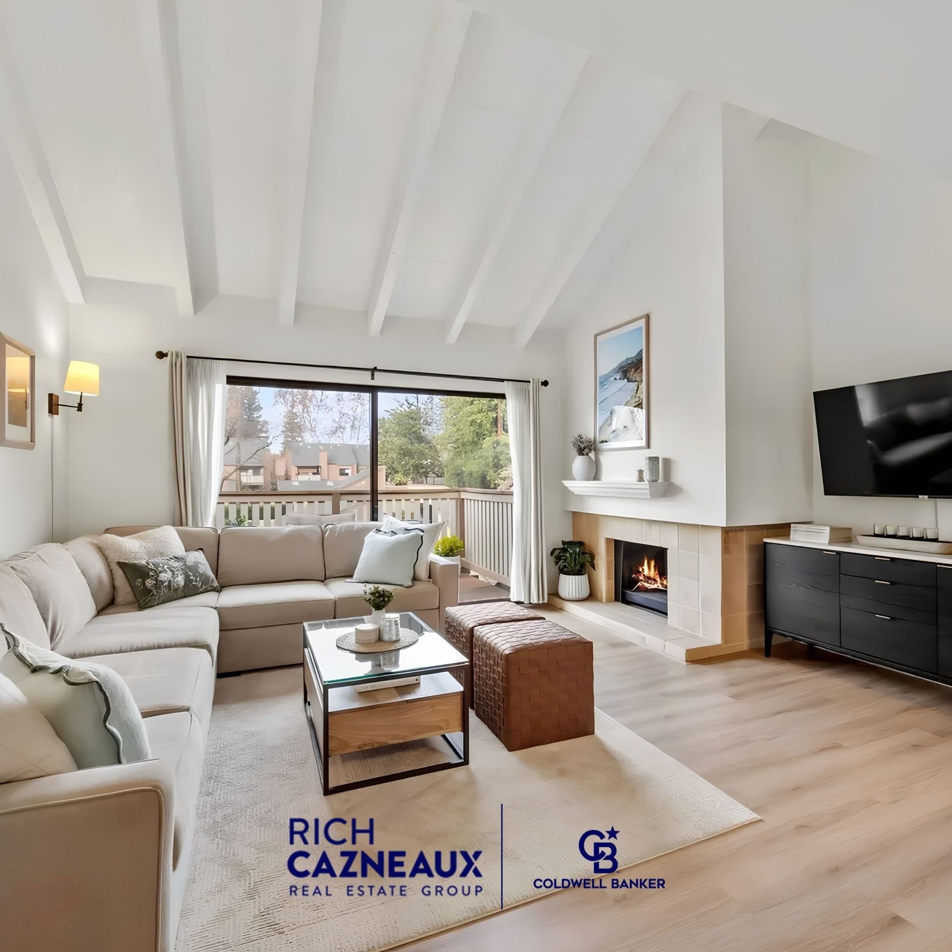 Living room with beam ceiling sectional and fireplace featuring Rich Cazneaux Real Estate Group and Coldwell Banker logos.