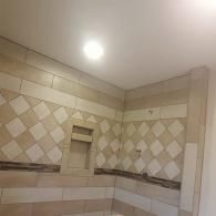 Shower wall with tan and cream rectangular and diamond-patterned tiles and a built-in recessed storage niche.