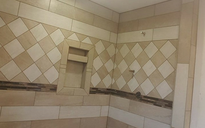 A shower wall tiled with a diagonal checkered pattern, horizontal strips, and a built-in recessed shelf niche.
