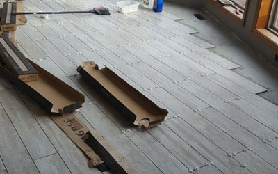 Light gray wood-look tiles are being installed on a floor, with tile spacers visible between the planks.
