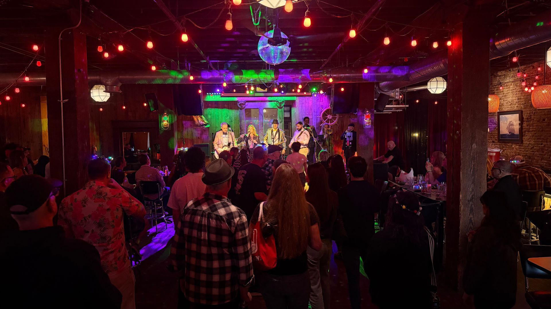 Crowded nightclub dance floor with red and purple lights and a live band on stage