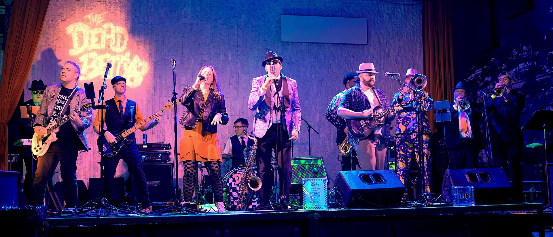 Live band performing on a blue-lit stage with multiple musicians and instruments