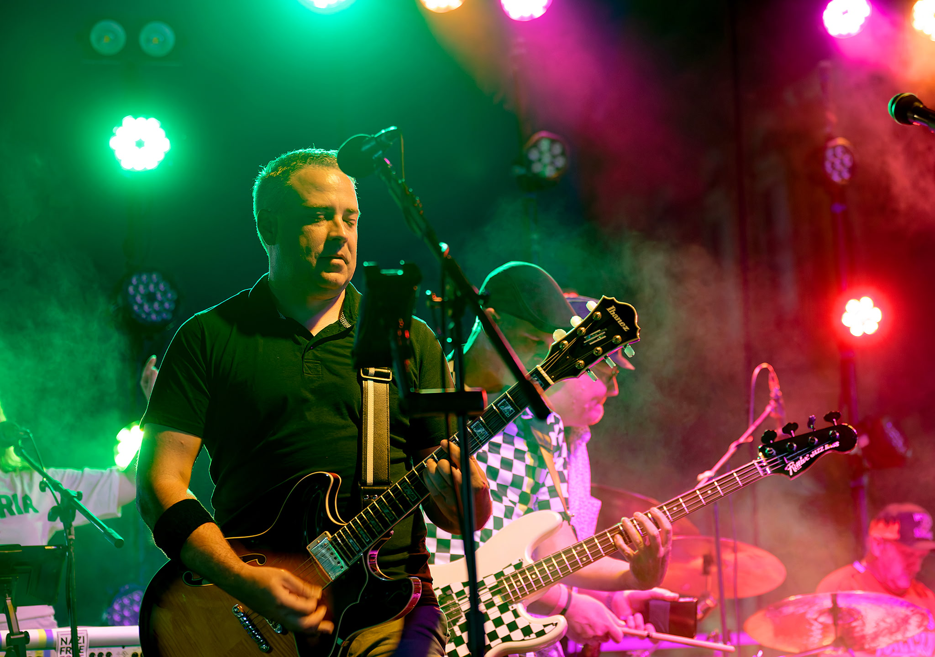 Two musicians performing onstage under colorful lights, one singing into a microphone and playing guitar.
