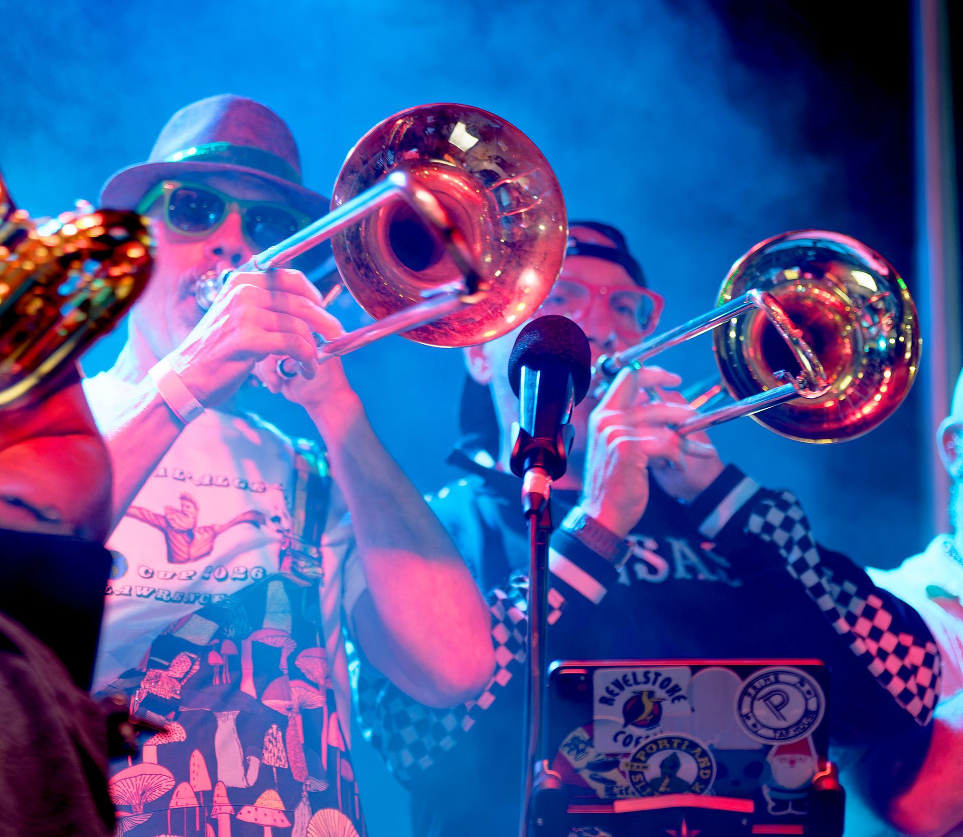 Two trombone players performing on a blue-lit stage with a microphone in front