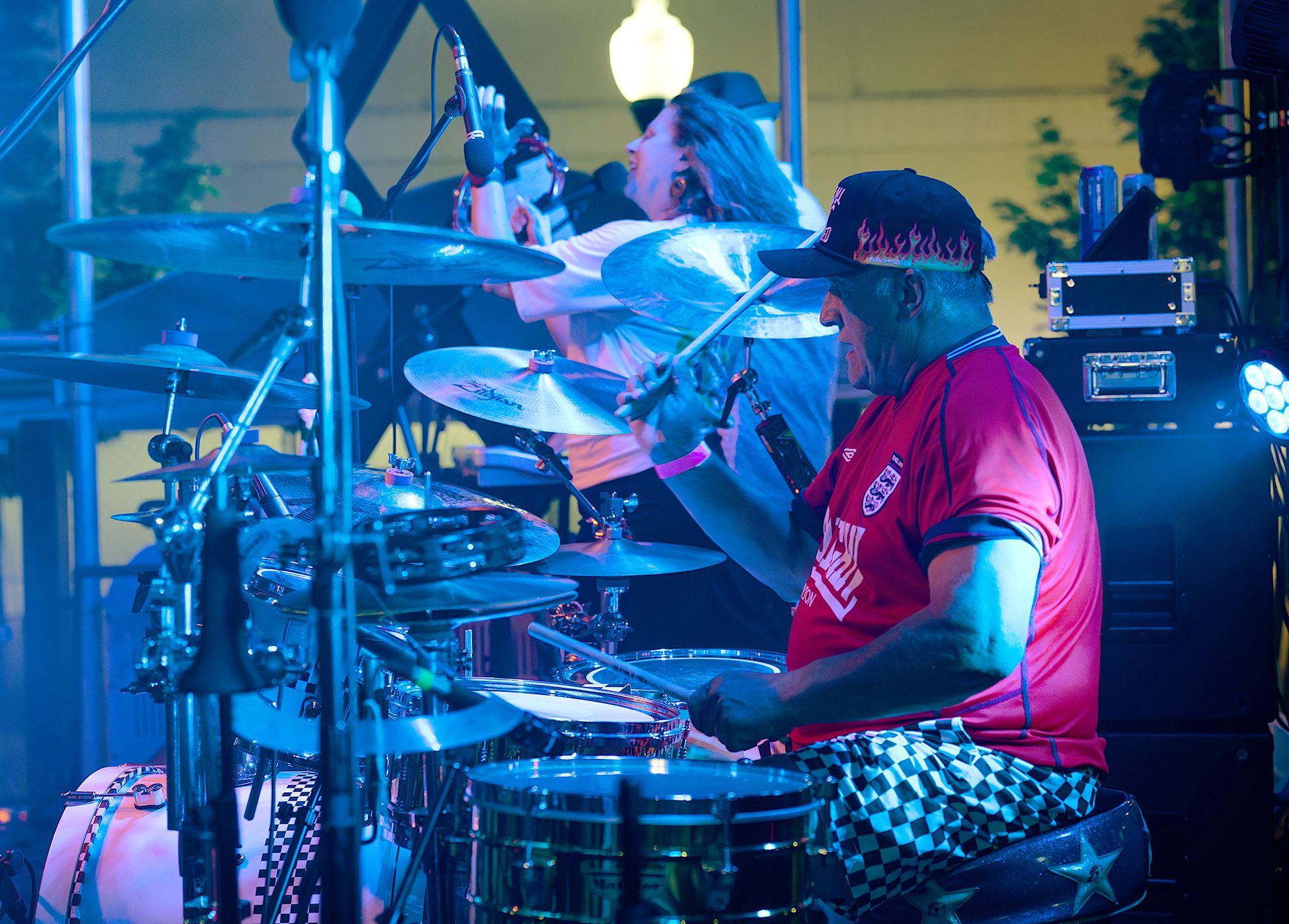 Drummer in red shirt playing on a lit stage during a live concert