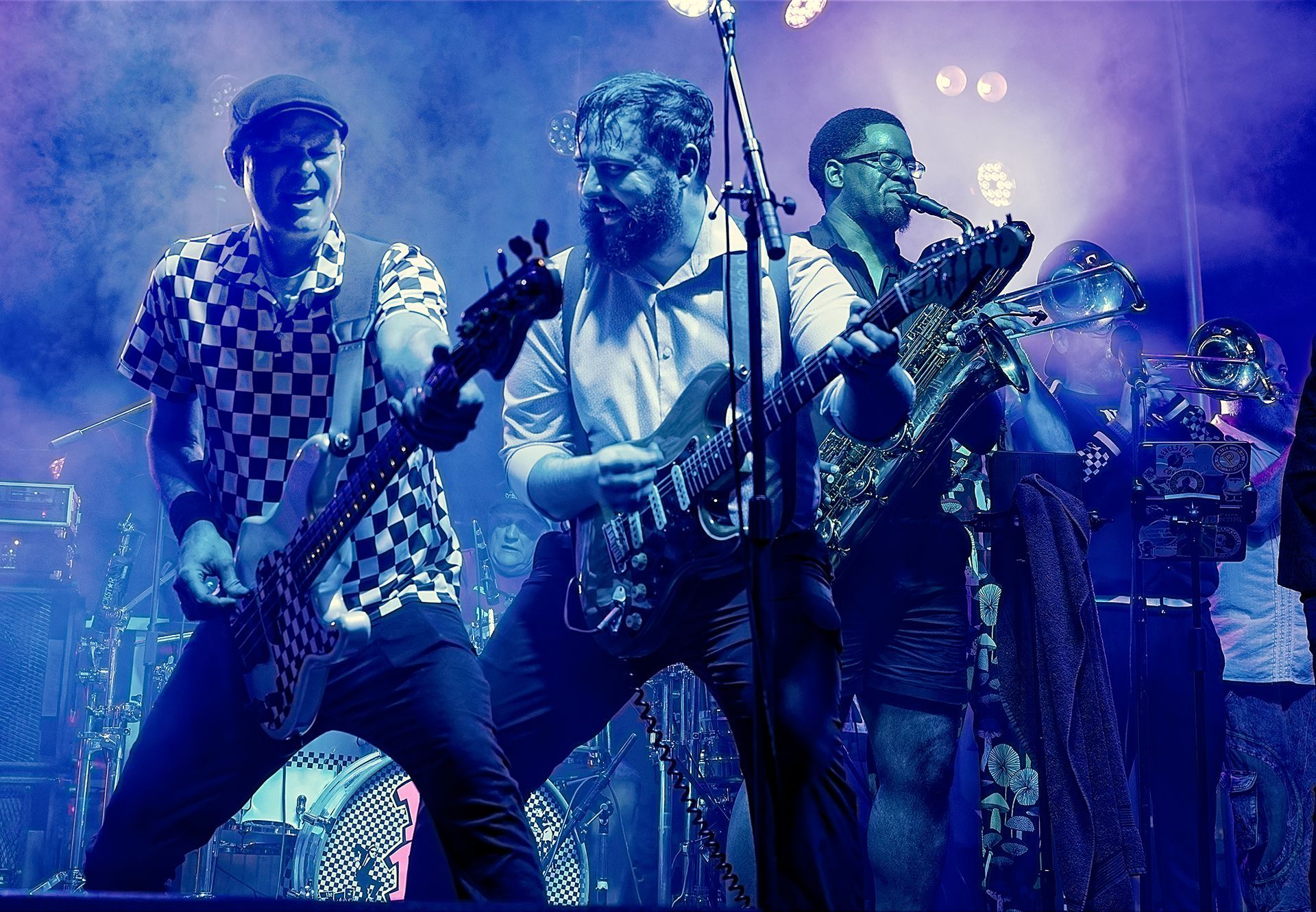 Band performing on stage under blue and purple lights, playing guitars and singing into microphones.