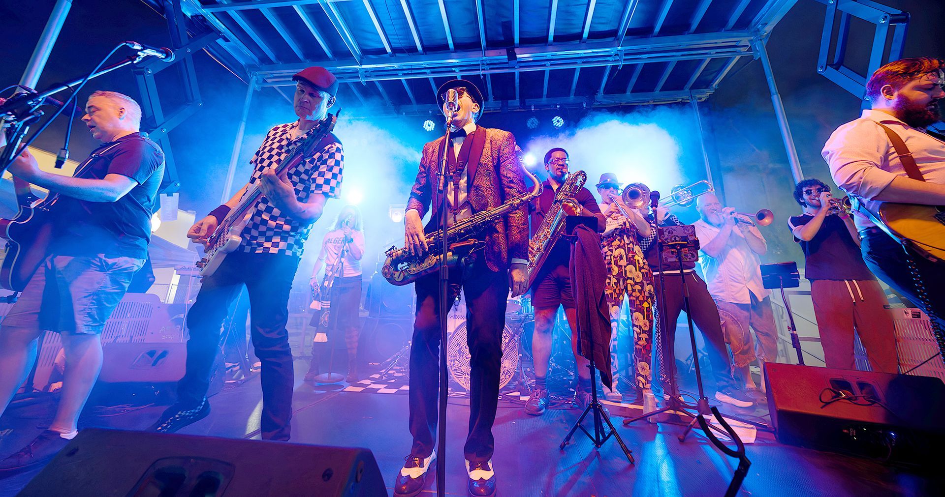 Band performing on a neon-blue lit stage with guitars and microphones.