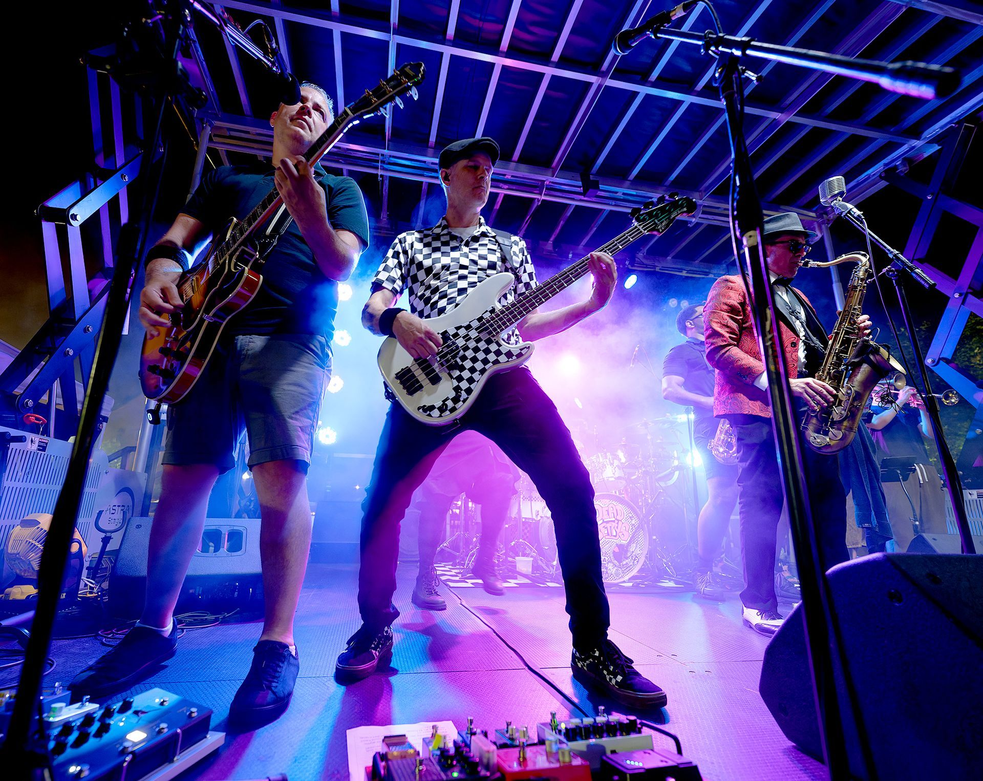 Three musicians performing onstage under blue and purple lights, playing guitars and singing into microphones
