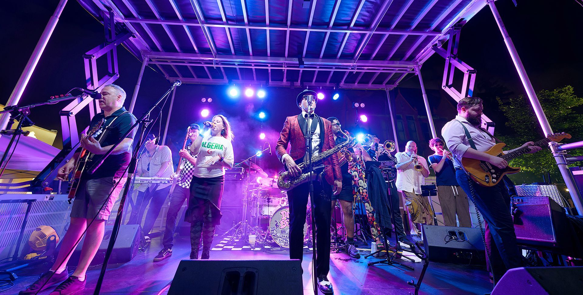 Live band performing on a lit outdoor stage with purple and blue lights at night