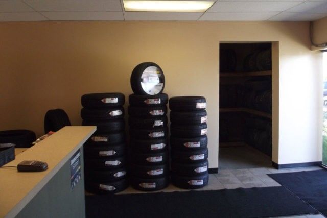 Tire shop lobby with stacked tires, a counter, and an open doorway to a storage room.