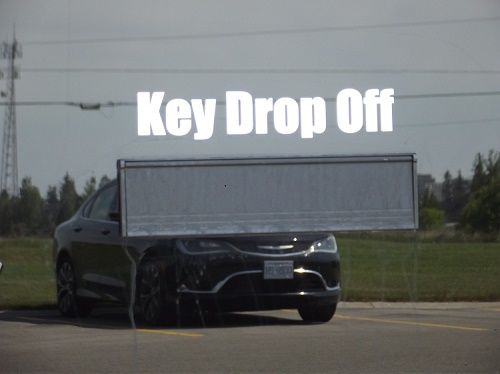 A key drop-off sign on a road near an industrial field