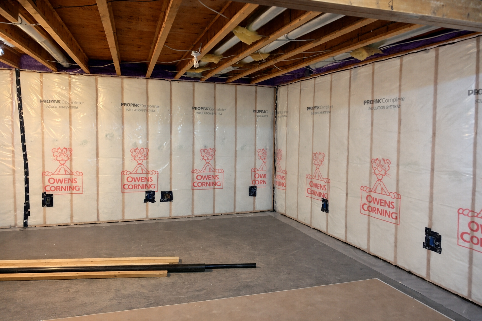 Basement interior with insulated walls and exposed ceiling beams, ready for finishing.