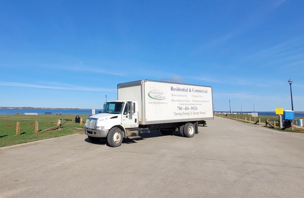 White Energy Savers Insulation box truck parked on a paved road near a body of water and a grassy area under a blue sky.