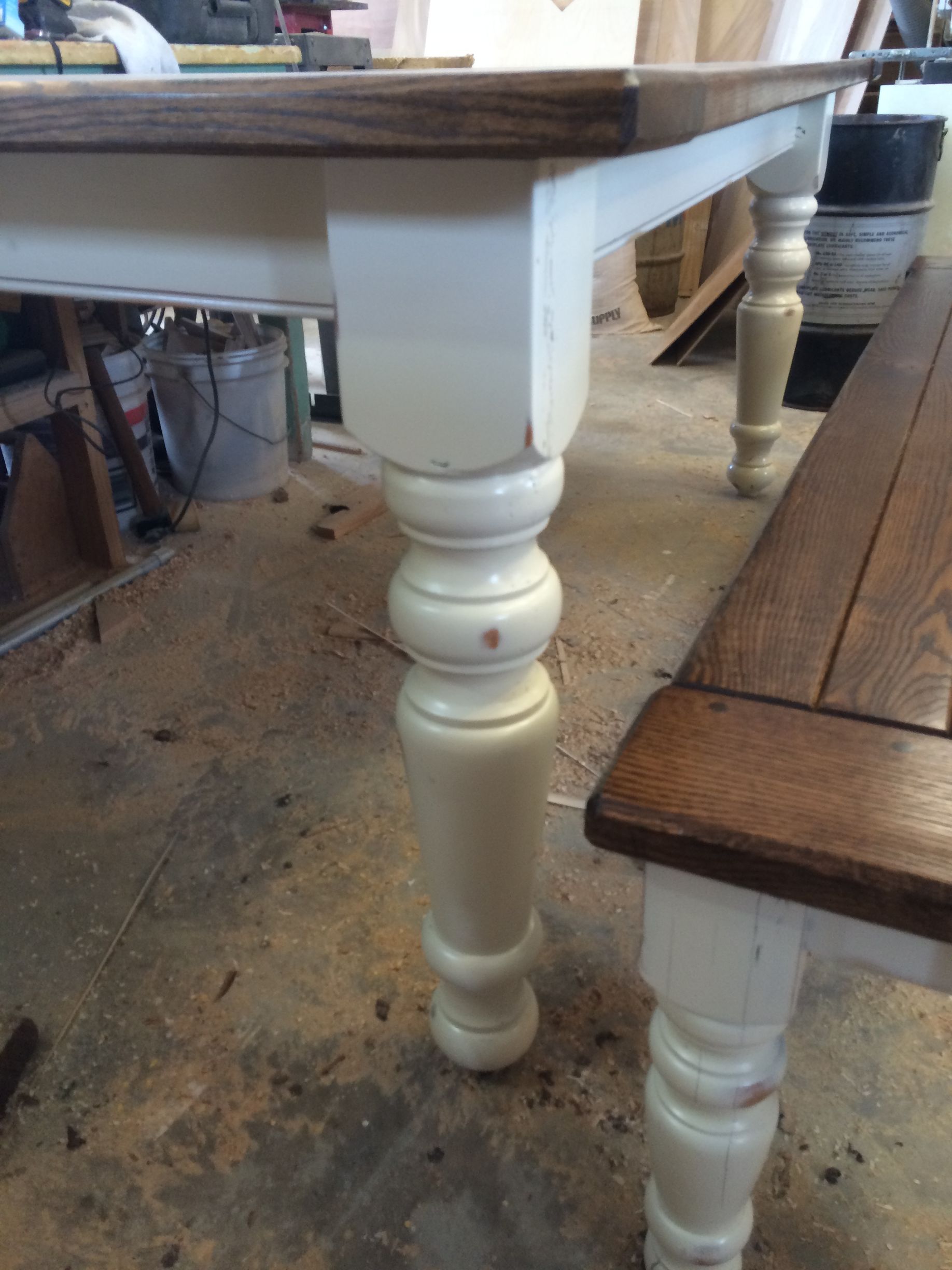 A wooden table with white legs is sitting next to a wooden bench.