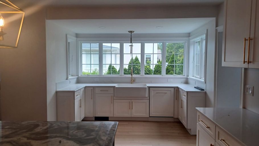 Bright white kitchen with a large window, L-shaped countertops, and light wood flooring