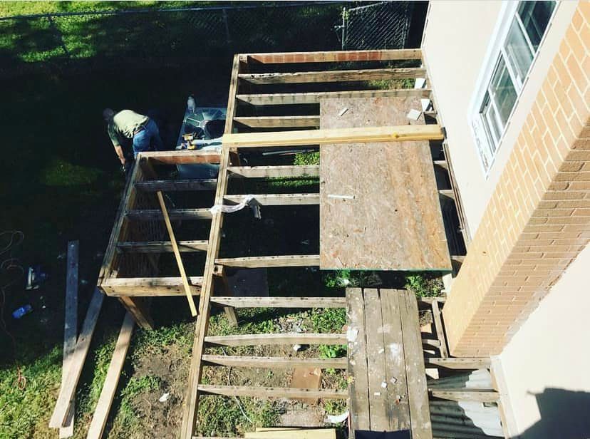 Wooden porch stairs and platform under construction beside a brick house, with tools and boards nearby