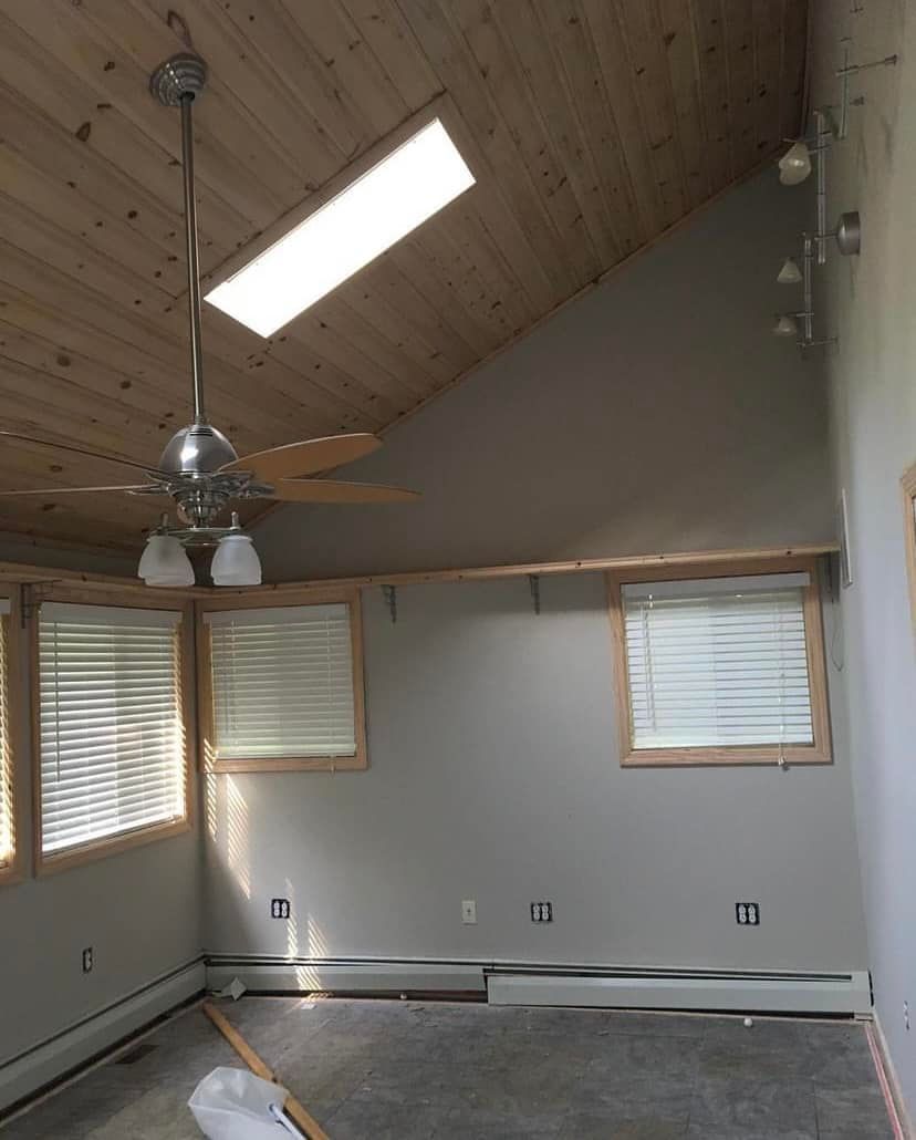 Empty room with slanted wood ceiling, skylight, ceiling fan, and small windows with blinds.